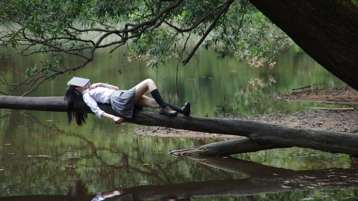 introvert lazy girl enjoying alone time laying on a tree brach at the lake